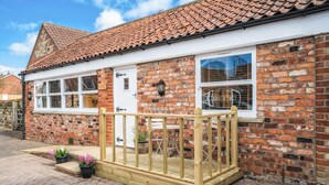 A brick building with a tiled roof, white-framed windows, and a wooden porch with a railing. - The Old Tractor Shed (Driffield)
