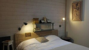 A bedroom with a wooden headboard, a bedside table, a lamp, and a framed picture on the wall. - Vintage Touch (Hannonville-sous-les-Côtes)