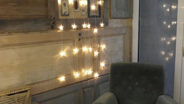 A rustic room with a wooden wall, a dark green armchair, a wooden table, and string lights. - Vintage Touch (Hannonville-sous-les-Côtes)