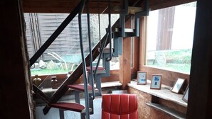 Un interior de madera con una silla roja, una escalera y cuadros en un estante.