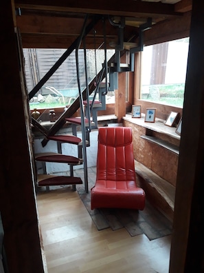 A wooden interior with a red chair, a staircase, and framed pictures on a ledge.