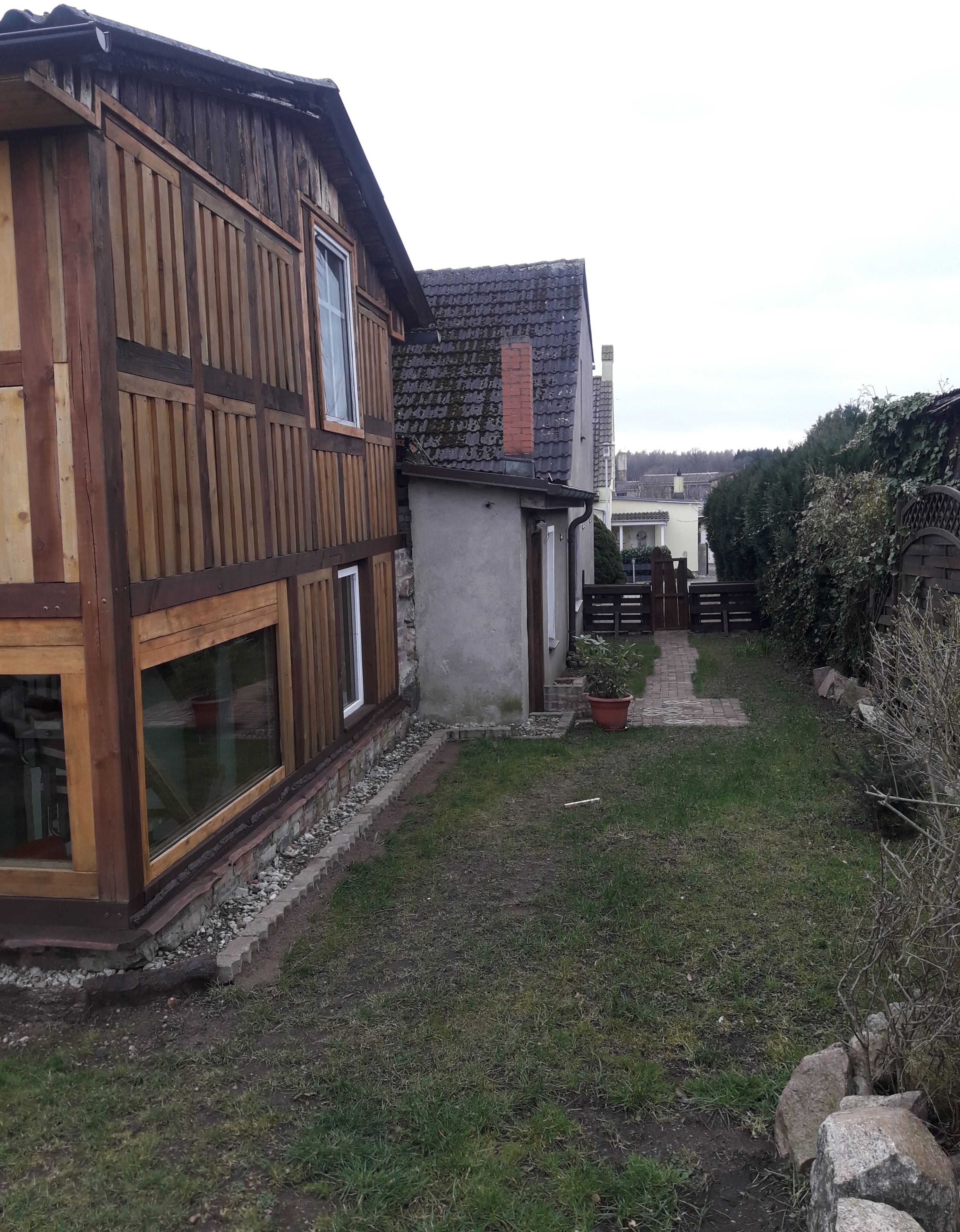 Una casa de madera con ventanas grandes y un camino empedrado que lleva a un portón.