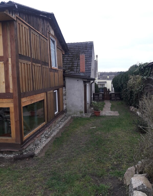 A wooden house with large windows and a paved pathway leading to a gate.