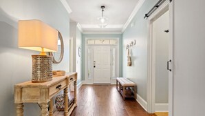 A hallway with wooden flooring, a wooden console table with a lamp, a bench, and a door at the end. - Beach Bliss: Beach Minutes Away, 6-Seater Golf Cart, and Sparkling Resort Pool! (Santa Rosa Beach)