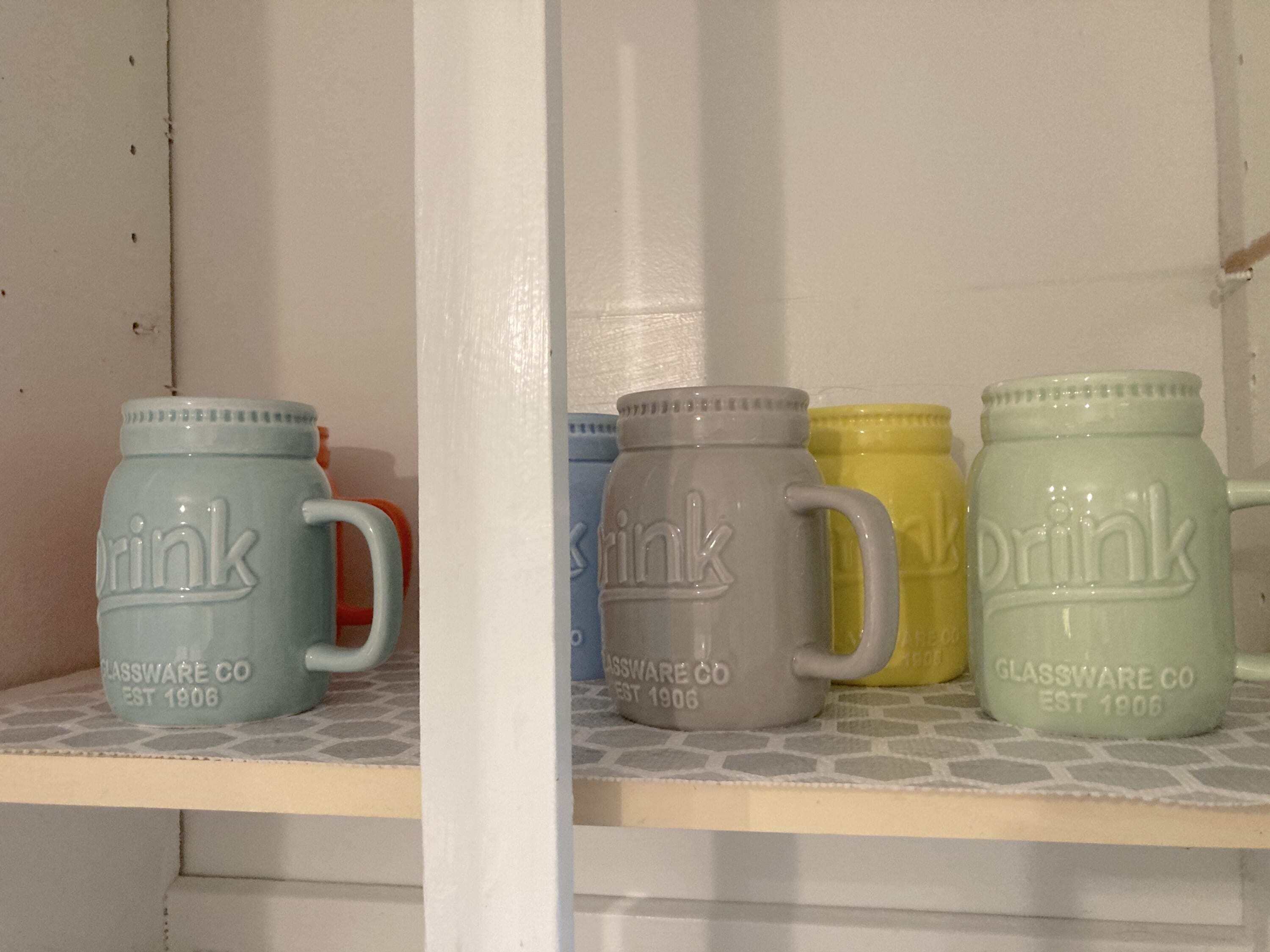 Een plank met vier keramische mokken waarop 'drink' en 'Glassware Co EST 1906' staat.