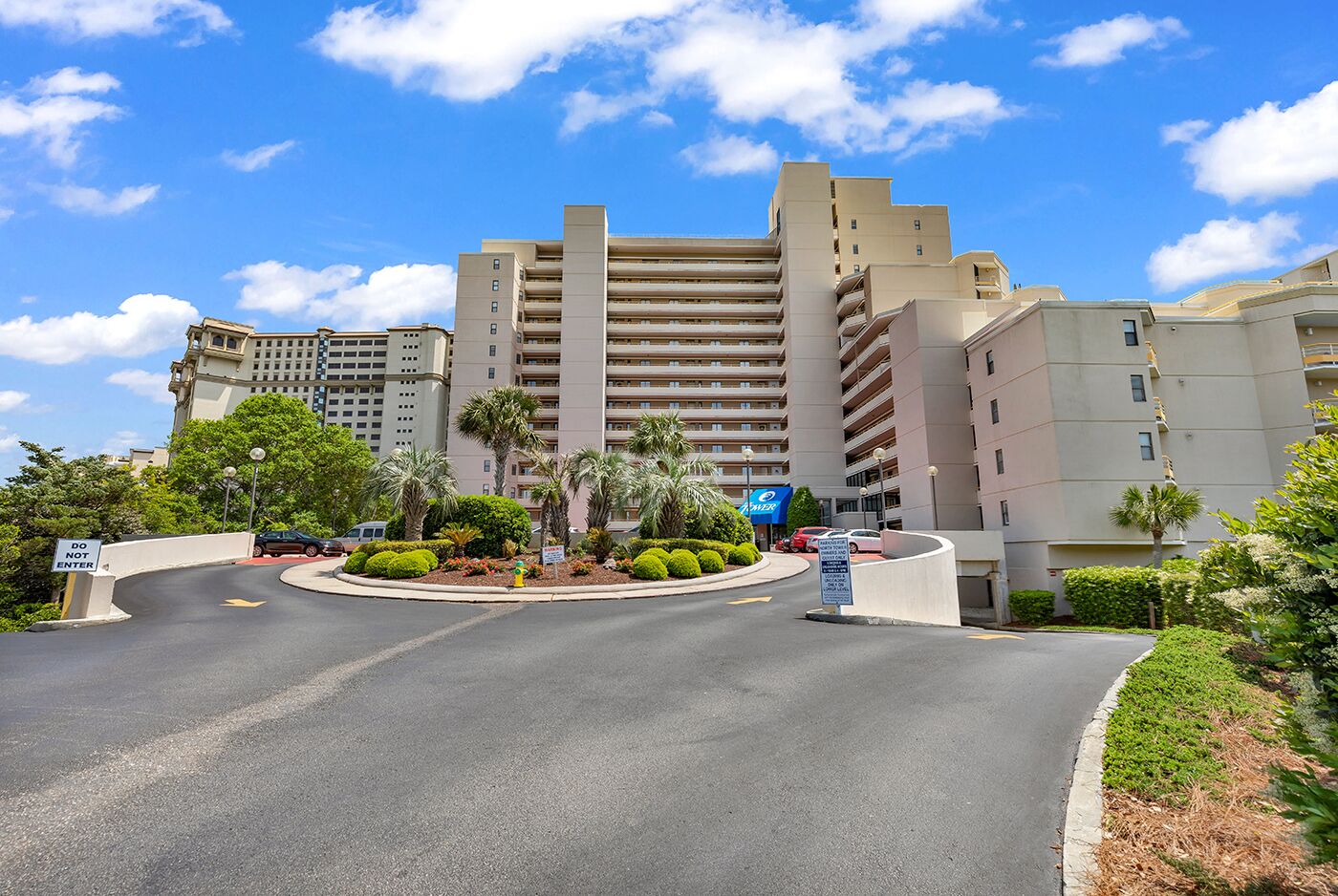 A multi-story hotel with a central courtyard, palm trees, and a clear blue sky.