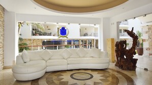 Un lobby moderno con un sofá seccional de cuero blanco, una escultura de madera decorativa y un suelo con estampado geométrico.