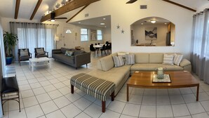 A spacious living room with a large sofa, a coffee table, and a dining area in the background. - Castaway Cottage - Private Beach Walkway, Beautiful Views, Ping Pong Table! (St. Augustine)