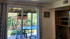 A bedroom with a bed, a wooden cabinet, a chandelier, and a view of an outdoor deck with a table and chairs. - Castaway Cottage - Private Beach Walkway, Beautiful Views, Ping Pong Table! (St. Augustine)