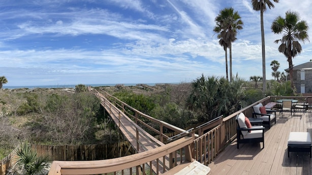 A wooden deck with outdoor furniture, a wooden walkway, and palm trees. - Castaway Cottage - Private Beach Walkway, Beautiful Views, Ping Pong Table! (St. Augustine)