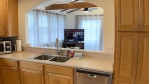 A modern kitchen with wooden cabinets, a stainless steel dishwasher, a double sink, and a built-in oven. - Castaway Cottage - Private Beach Walkway, Beautiful Views, Ping Pong Table! (St. Augustine)