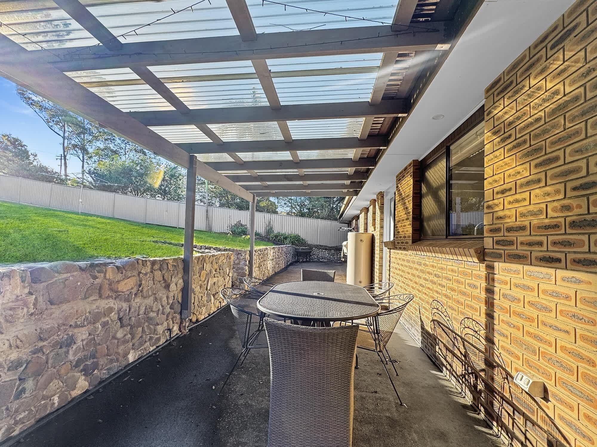 Ein überdachter Patio-Bereich mit einer Steinmauer, einer Ziegelwand mit Namensschildern und einem Tisch mit Stühlen.