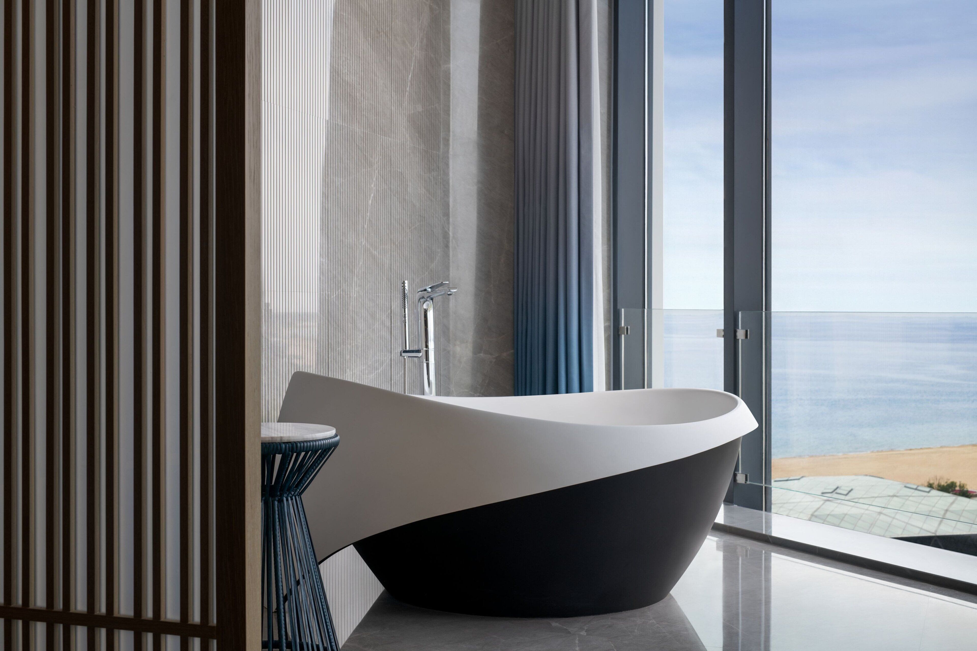 A modern bathroom with a freestanding bathtub, a round mirror, and a view of the ocean through large windows.