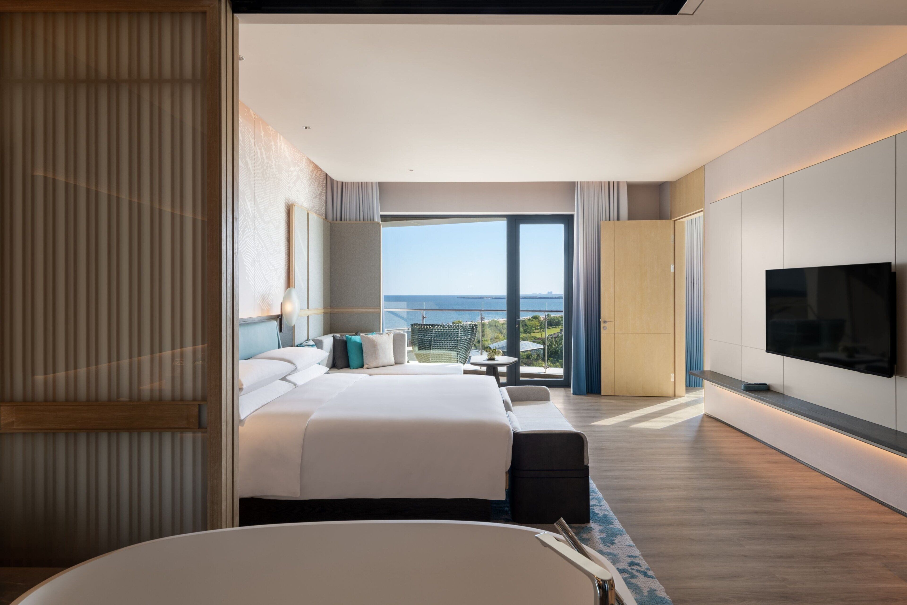 Ein modernes Hotelzimmer mit einem großen Bett, einem Fernseher und einem Balkon mit Meerblick.