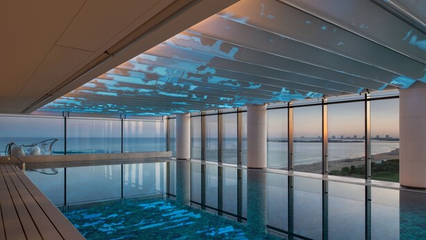 A modern infinity pool with a city view, large windows, and a wooden deck. - Qinhuangdao Marriott Resort (Qinhuangdao)