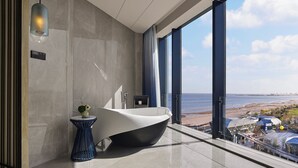 A modern bathroom with a large bathtub, a small table with a vase, and a view of the beach through large windows. - Qinhuangdao Marriott Resort (Qinhuangdao)