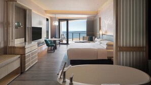 A modern hotel room with a large bed, a sitting area with a TV, and a view of the sea. - Qinhuangdao Marriott Resort (Qinhuangdao)