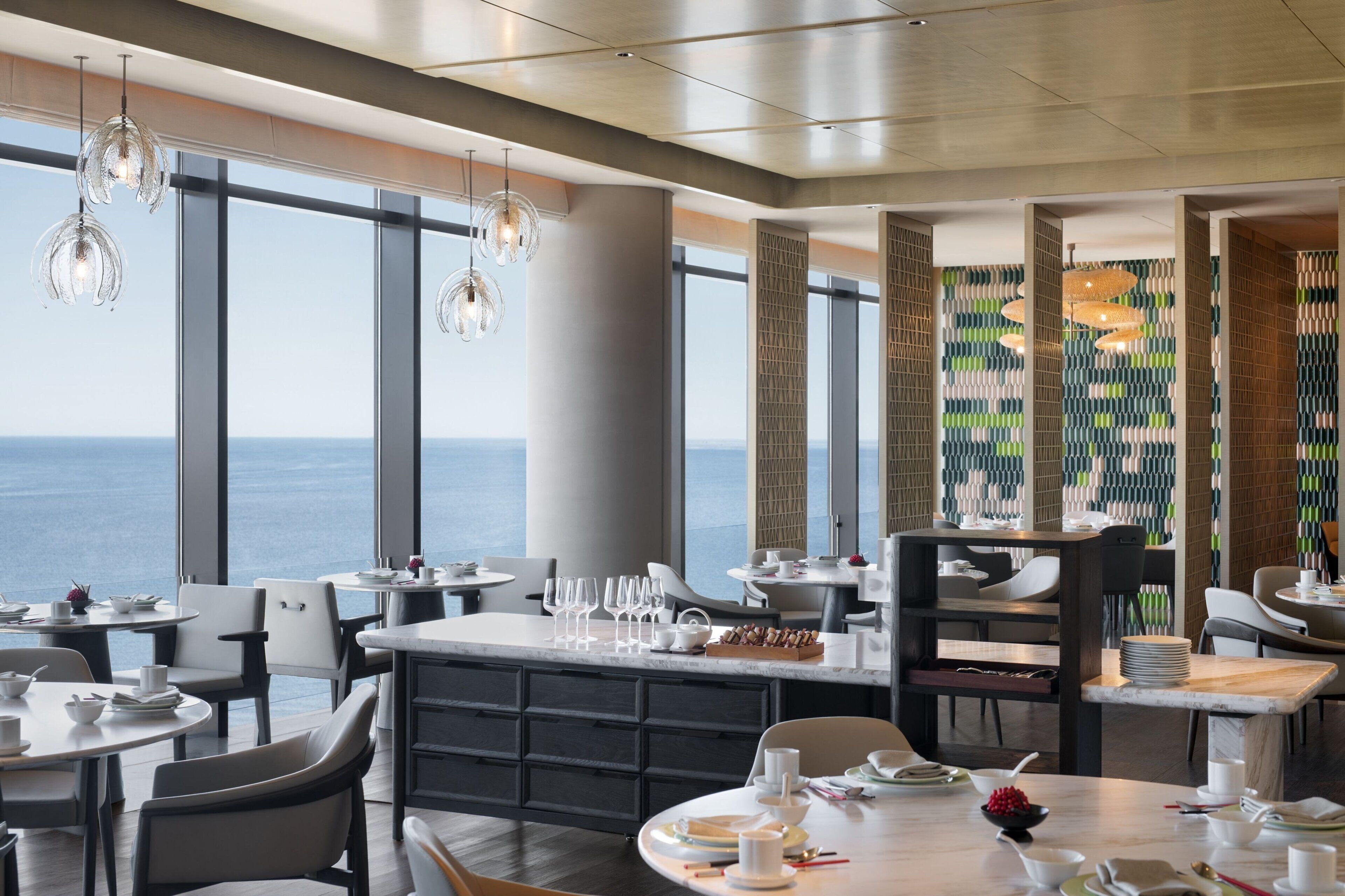 A modern dining area with large windows, a central island, and hanging pendant lights.