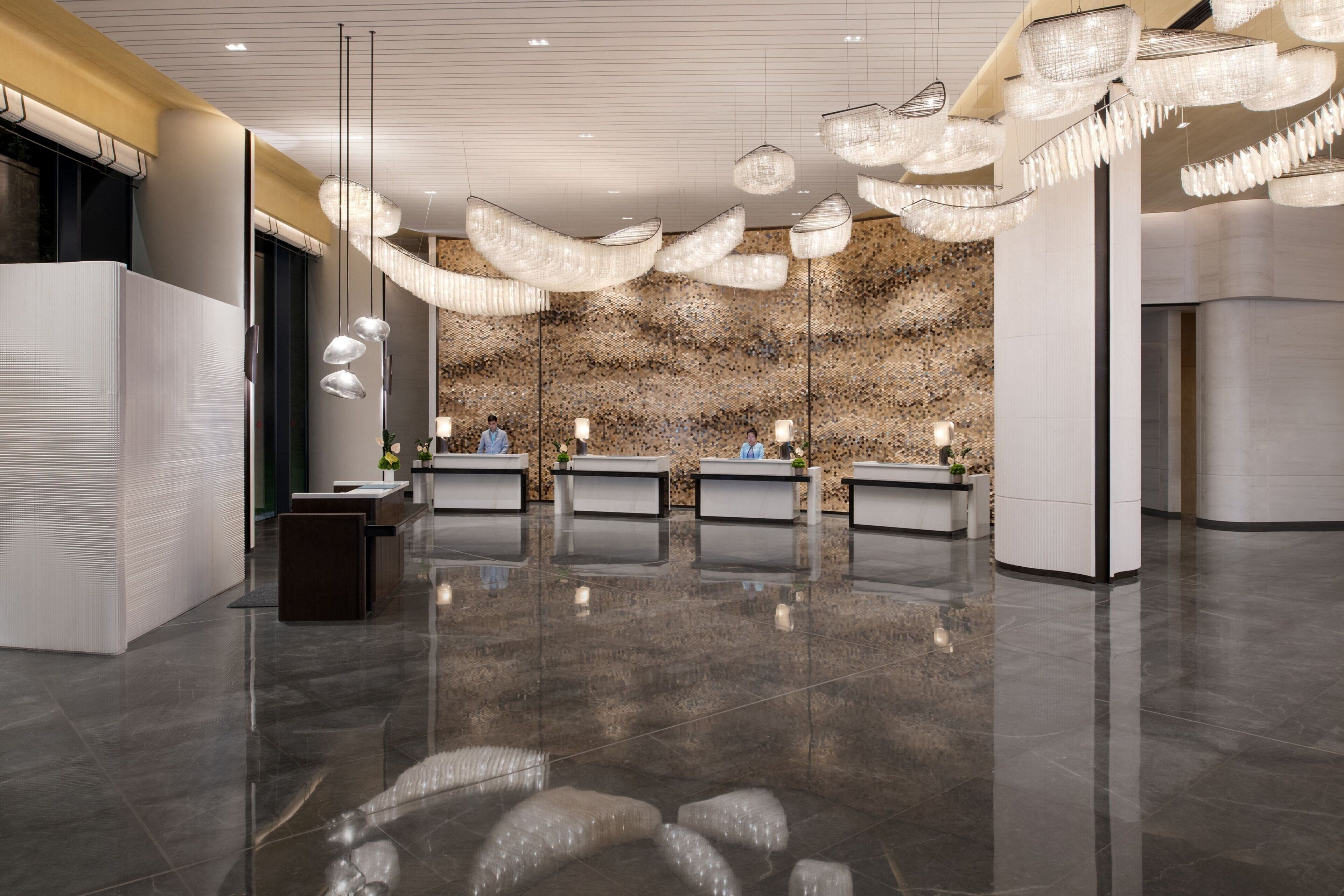 A modern reception area with a polished floor, multiple reception desks, and hanging chandeliers.