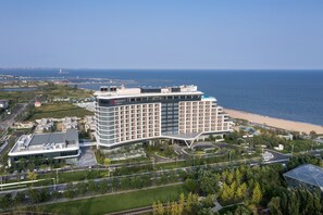A modern hotel with a large glass facade, located near a beach with a view of the sea. - Qinhuangdao Marriott Resort (Qinhuangdao)