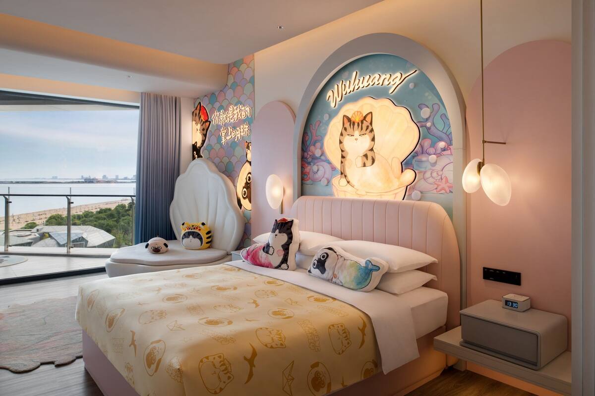 A modern bedroom with a large bed, a view of the city, and a mural of a cat on the wall.