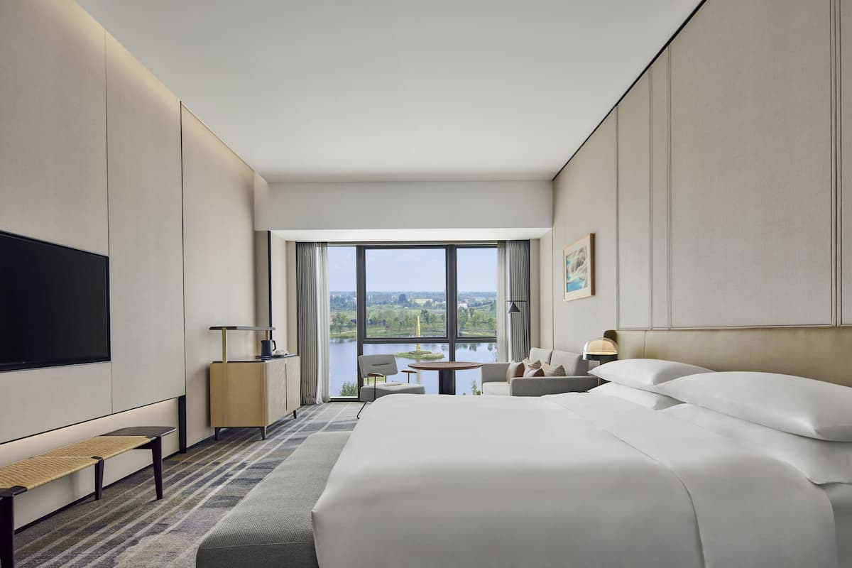 Ein modernes Hotelzimmer mit einem großen Bett, einem Flachbildfernseher, einem Schreibtisch und Blick auf einen See.