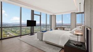 Ein modernes Hotelzimmer mit einem großen Bett, einem Flachbildfernseher, einem Schreibtisch und Blick auf die Stadt.