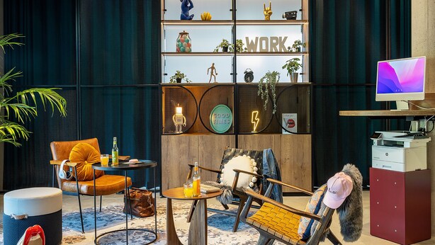 A modern workspace with a desk, chairs, and a bookshelf with decorative items.