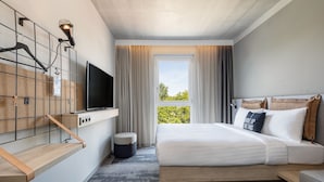 A modern hotel room with a bed, a TV mounted on a wall, a small table, and a window with curtains.