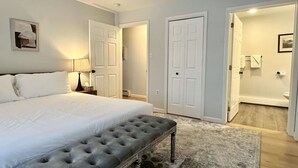 A bedroom with a large bed, a bench, a nightstand, and a door leading to a bathroom. - Pondside View Family Friendly Home!  [Moose Lodge] (Bar Harbor)