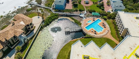 Vista aérea de un hotel frente al mar con piscina, acceso directo a la playa y un pequeño puerto deportivo.