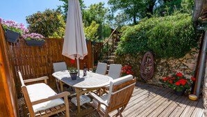 A wooden deck with a round table and chairs, surrounded by a wooden fence and potted plants.