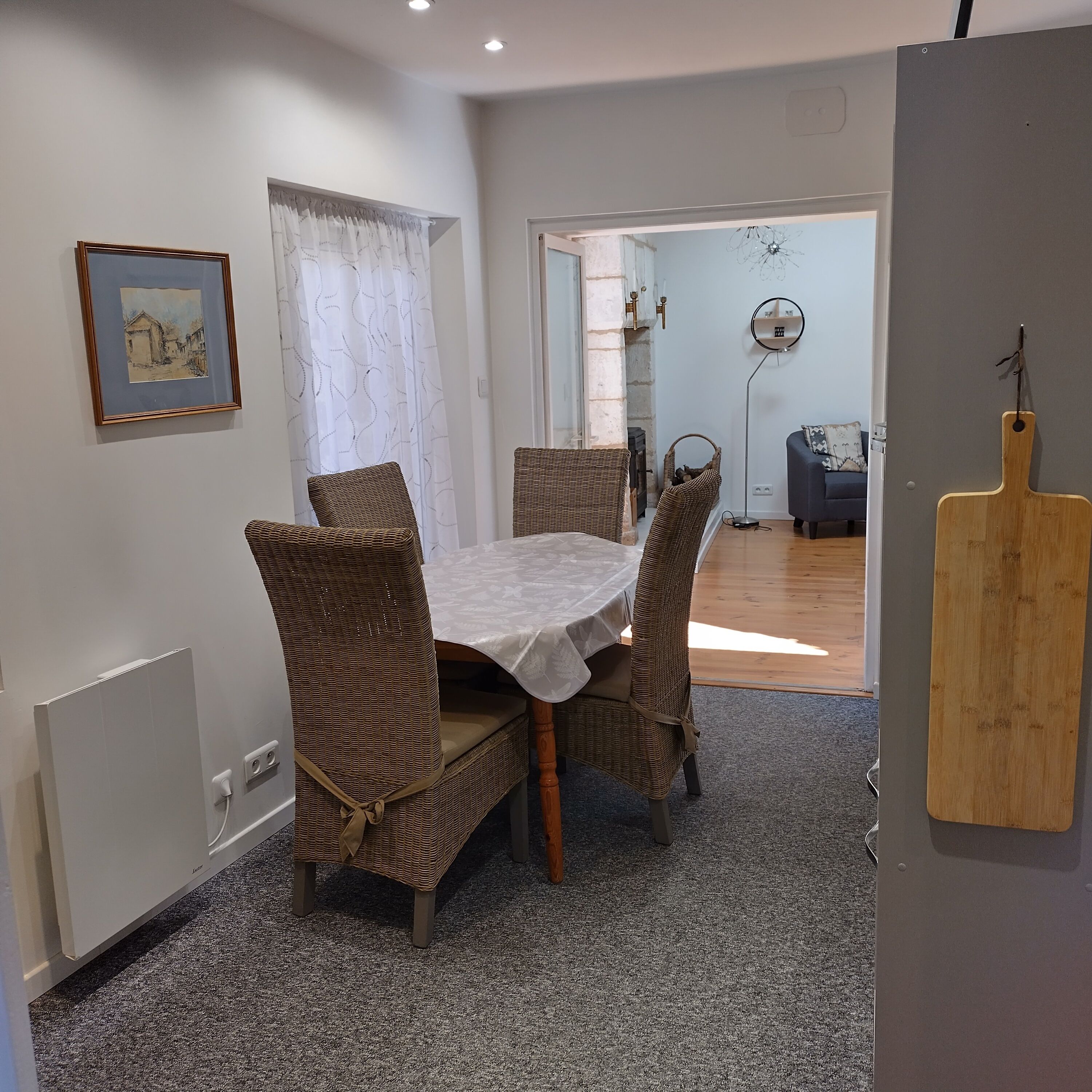 A dining area with a table and chairs, a framed picture on the wall, and a wooden board on the wall.