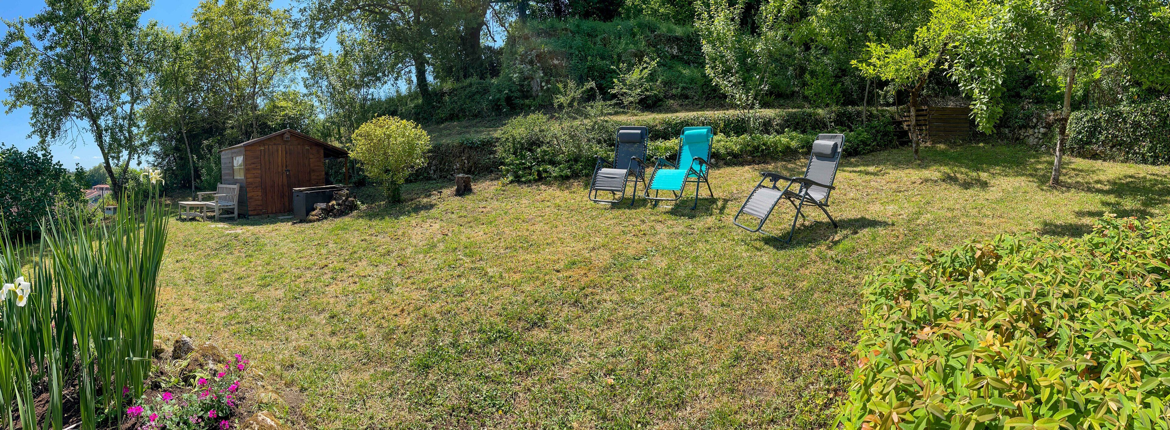 Un espace extérieur verdoyant avec un abri en bois, deux fauteuils de jardin et une petite table.