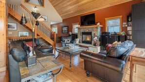 A spacious living room with a fireplace, leather sofas, a coffee table, and a wooden staircase. - 3 Bears Cabin | Games Room | Firepit | Lux Kitchen (Invermere)