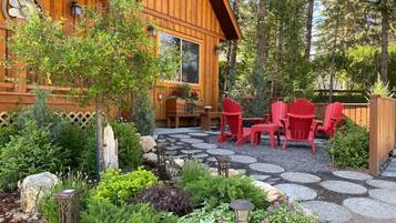 Une cabane en bois avec un patio en pierre, des fauteuils Adirondack rouges et une variété de plantes.