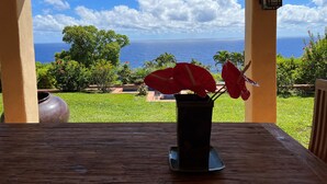 A wooden table with a vase of red flowers, set against a backdrop of a clear blue sky and ocean view. - 6.5 acres Oceanfront Estate with180-degree views of the deep blue Pacific Ocean! (Ninole)