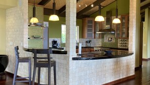 A spacious kitchen with a central island, pendant lighting, and exposed brick ceilings. - 6.5 acres Oceanfront Estate with180-degree views of the deep blue Pacific Ocean! (Ninole)
