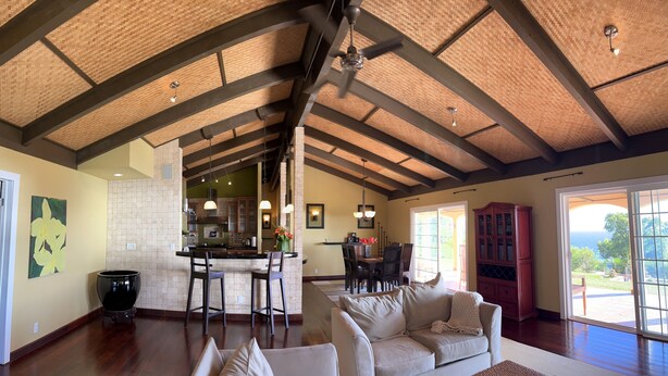 A spacious living area with a high ceiling, a kitchen in the background, and a view of the outdoors. - 6.5 acres Oceanfront Estate with180-degree views of the deep blue Pacific Ocean! (Ninole)