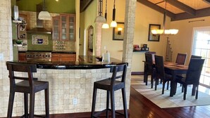 A kitchen with a central island, wooden chairs, and a dining table with chairs. - 6.5 acres Oceanfront Estate with180-degree views of the deep blue Pacific Ocean! (Ninole)