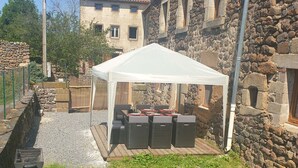 Un bâtiment en pierre doté d’un patio couvert d’une tente blanche, comprenant un espace extérieur avec des sièges et un barbecue.