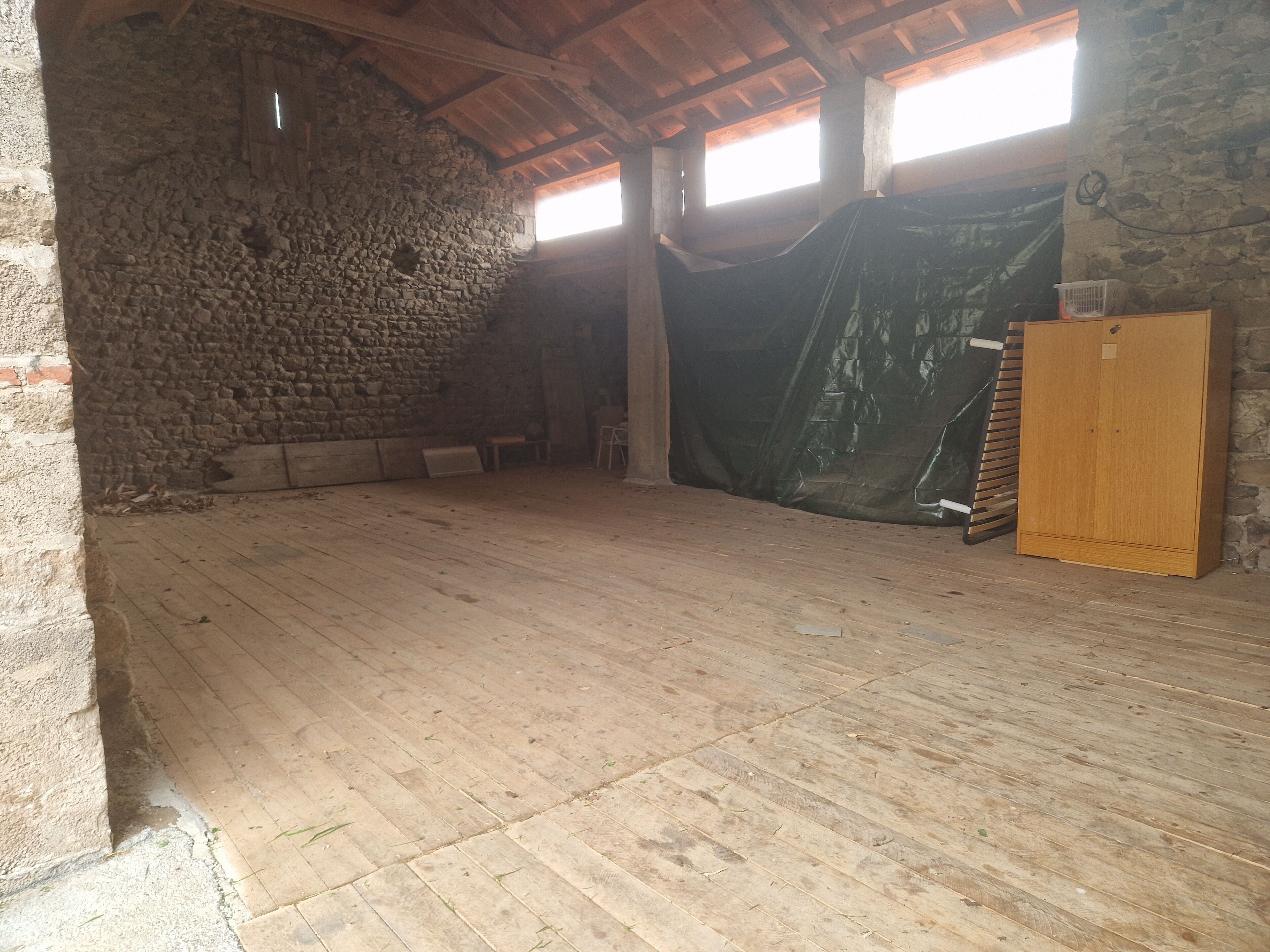 Une pièce rustique avec un mur en pierre, des poutres apparentes, un plancher en bois et une armoire en bois.