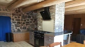 Une cuisine avec un mur en pierre, un poêle et un rideau bleu.