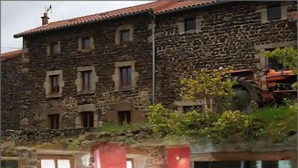 Un bâtiment en pierre doté d’une cheminée, d’une porte rouge et d’un canapé bleu.