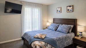 A bedroom with a bed, a TV mounted on the wall, a window with sheer curtains, and two wall art pieces. - Cozy Coastal Home, 2 Mi to Navarre Beach (Navarre)