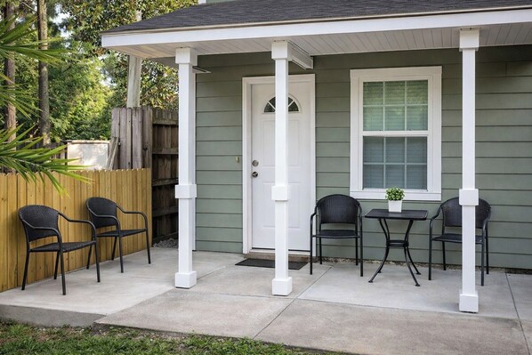 A porch with four chairs and a small table, a door, and a window.
