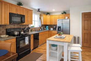 A modern kitchen with wooden cabinets, a stainless steel refrigerator, a microwave, a stove, and a sink.