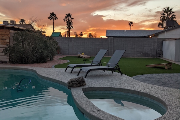 Backyard Oasis  with pool and hot tub. Turf lawn with Cornhole set up.