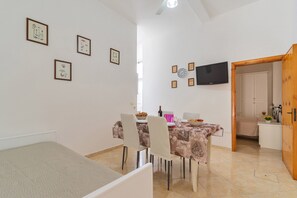 A dining area with a table set for four, chairs, a television mounted on the wall, and framed pictures on the wall.