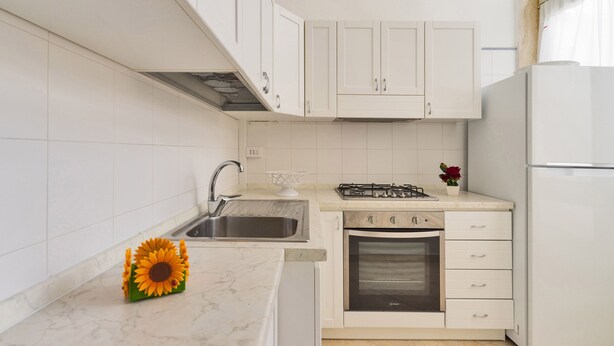 A modern kitchen with white cabinets, a stainless steel sink, a gas stove, and an oven.